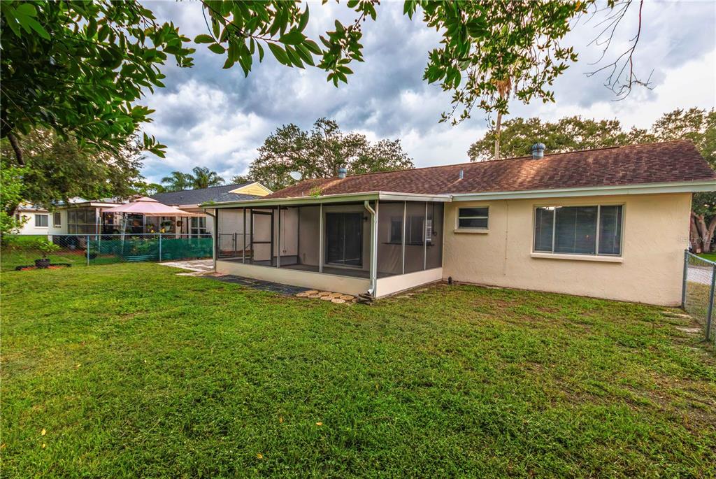 The backyard of a single-story house features a screened-in porch and a grassy lawn — 12401 GUNSTOCK LANE, HUDSON, FL