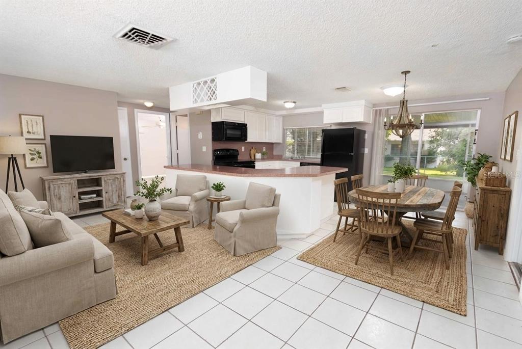 An open-concept living and dining area features white tile floors, beige furniture, and a kitchen — 12401 GUNSTOCK LANE, HUDSON, FL