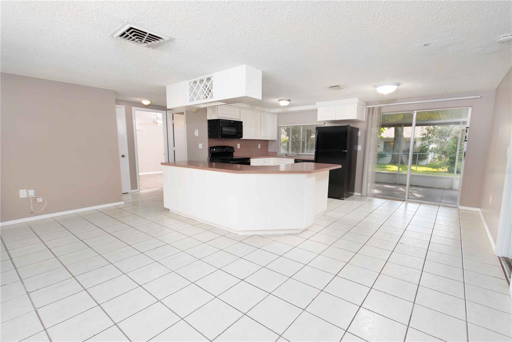 A kitchen with white cabinets, a peninsula, and tile flooring opens to a sliding door — 12401 GUNSTOCK LANE, HUDSON, FL