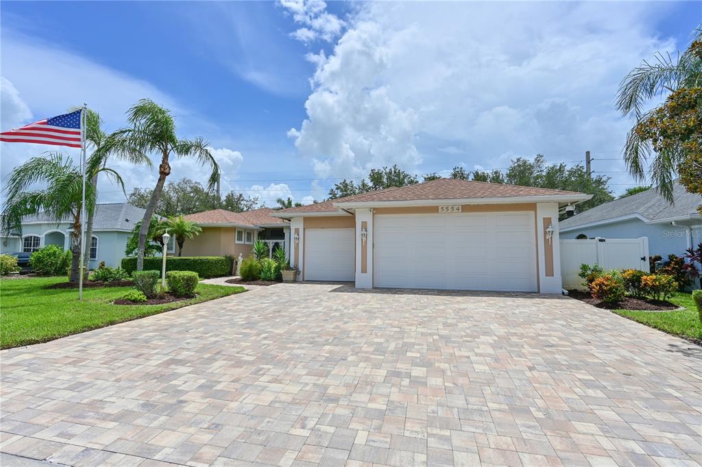 A single-story house features a paved driveway, a three-car garage, and an American flag — 5554 MAGNOLIA BLOSSOM LANE, SARASOTA, FL