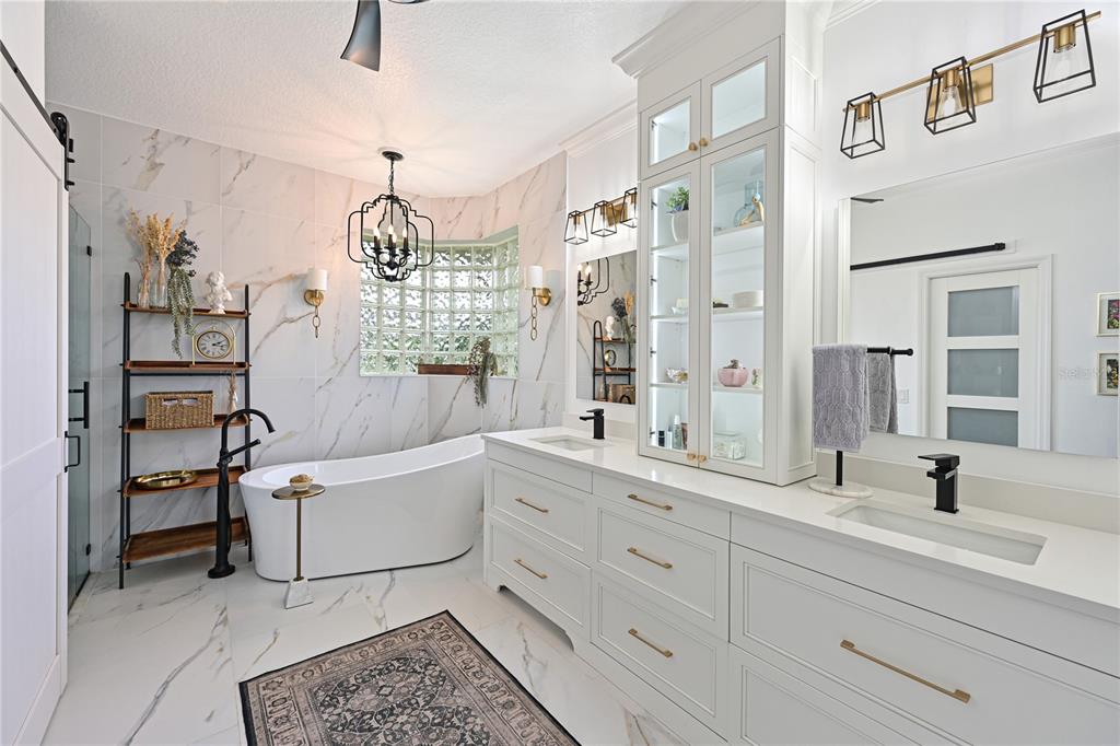 A luxury bathroom features a freestanding tub, double vanity, glass block window, and marble-look tile — 5554 MAGNOLIA BLOSSOM LANE, SARASOTA, FL