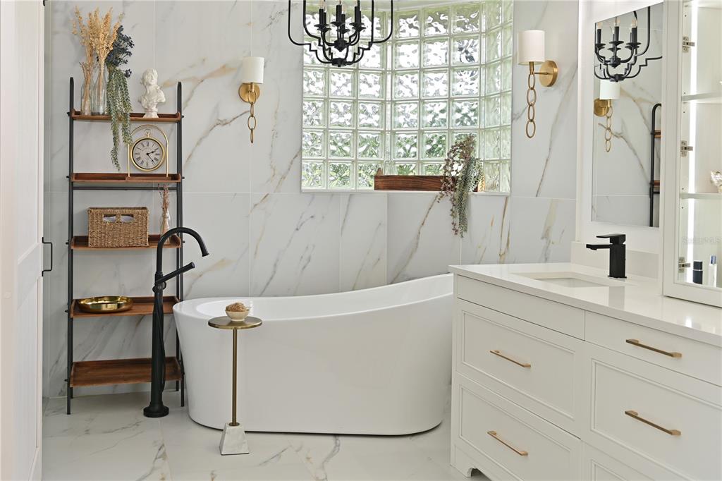 A modern bathroom features a freestanding tub, marble-look tile walls, and a glass block window — 5554 MAGNOLIA BLOSSOM LANE, SARASOTA, FL