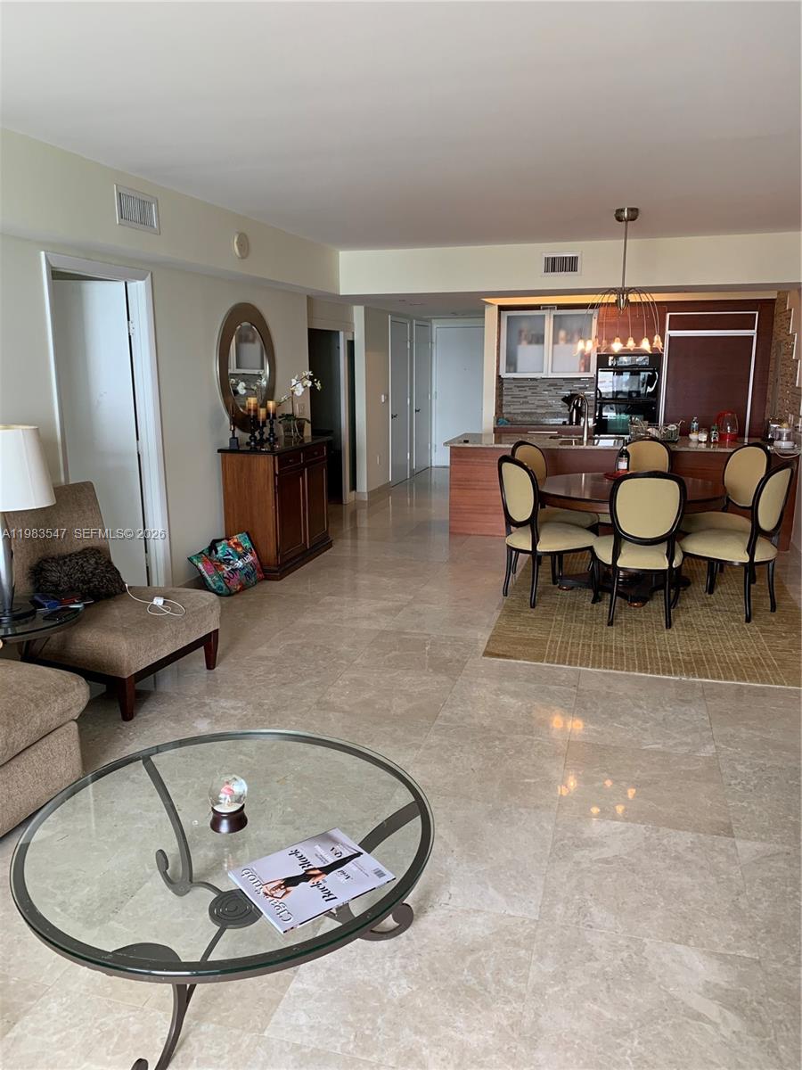 An open-concept living and dining area features tile flooring, a glass coffee table, and kitchen — 1830 S Ocean Dr # 2503, Hallandale Beach FL 33009, HALLANDALE BEACH, FL