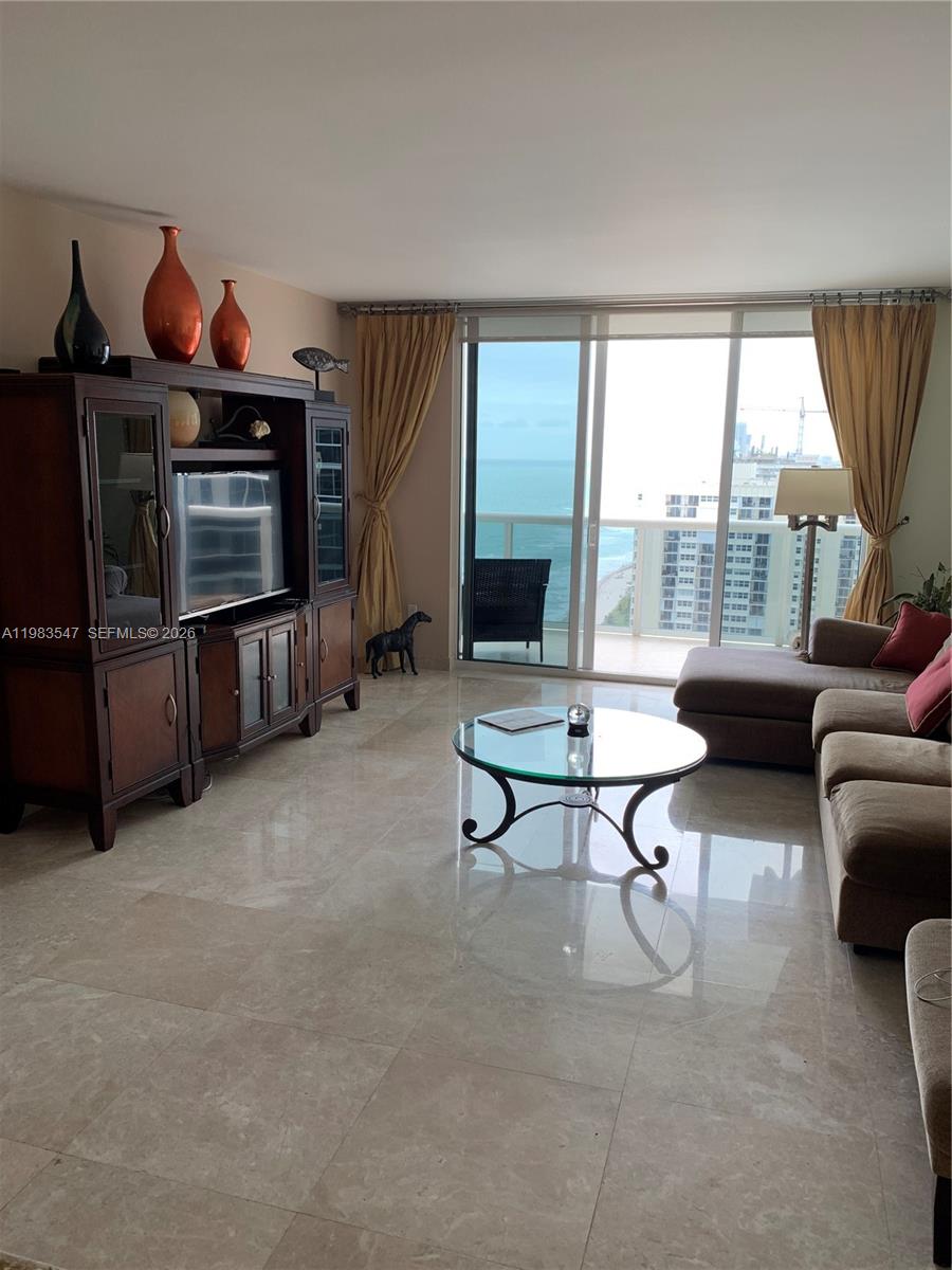 A living room features marble floors, a large entertainment center, and a balcony overlooking the ocean — 1830 S Ocean Dr # 2503, Hallandale Beach FL 33009, HALLANDALE BEACH, FL