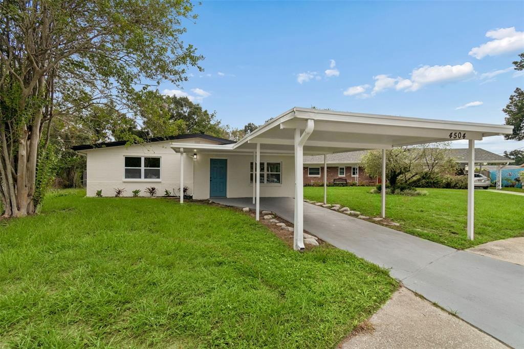 A white single-story house features a blue front door and an attached metal carport — 4504 ASHMORE DRIVE, TAMPA, FL