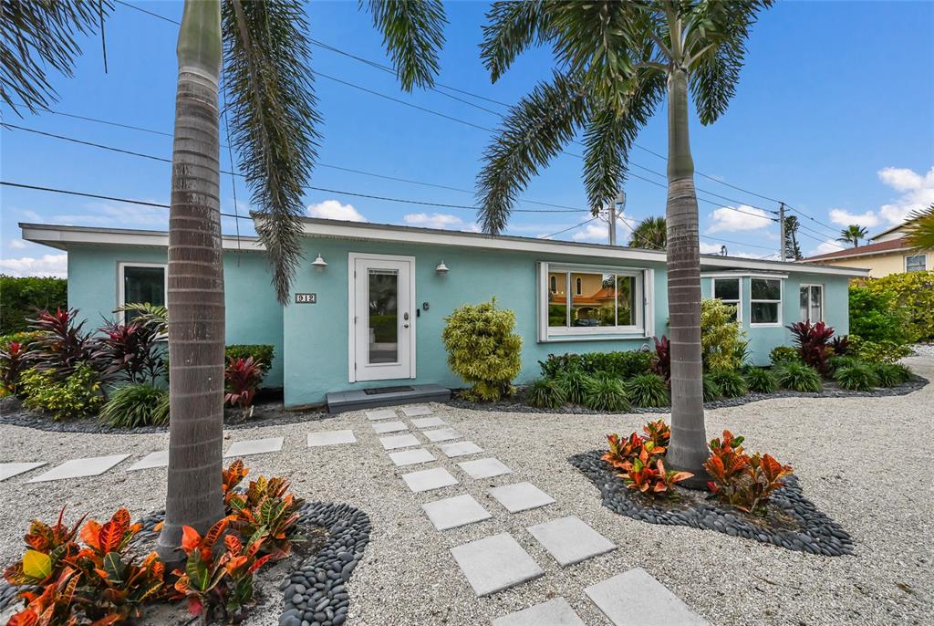 A light blue single-story house features a gravel yard, palm trees, and a stone walkway — 912 N SHORE DRIVE, ANNA MARIA, FL