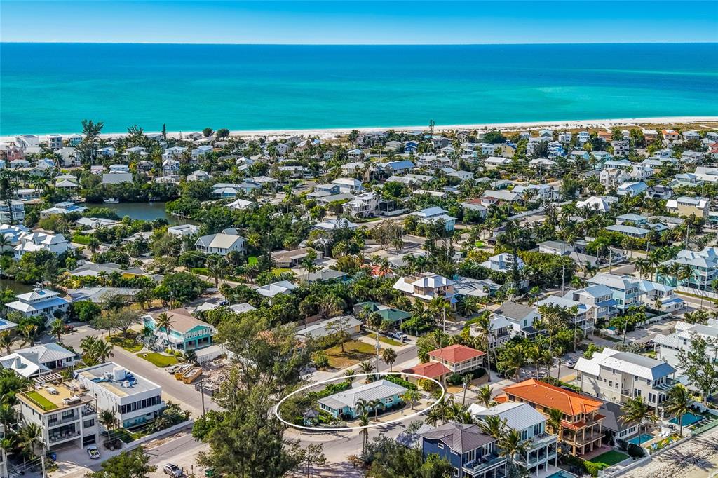 An aerial view shows a light blue house circled in a dense coastal residential neighborhood — 912 N SHORE DRIVE, ANNA MARIA, FL