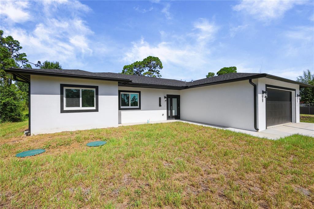 A single-story house with white stucco walls, black trim, and an attached garage — 828 GENOA AVENUE S, LEHIGH ACRES, FL
