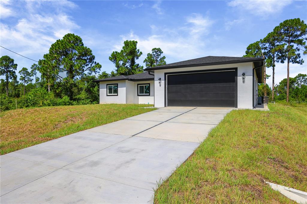 A white single-story house with a black garage door and roof sits on a grassy lot — 828 GENOA AVENUE S, LEHIGH ACRES, FL