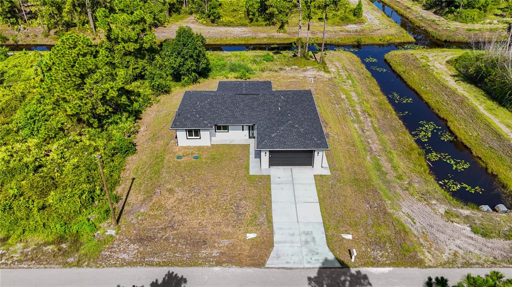 An aerial view shows a single-story house with a dark roof and driveway on a lot — 828 GENOA AVENUE S, LEHIGH ACRES, FL