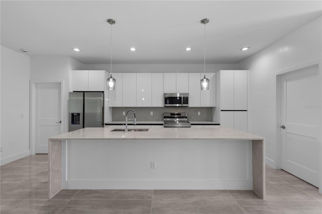 A modern kitchen features white flat-panel cabinets, stainless steel appliances, and a large waterfall island — 828 GENOA AVENUE S, LEHIGH ACRES, FL