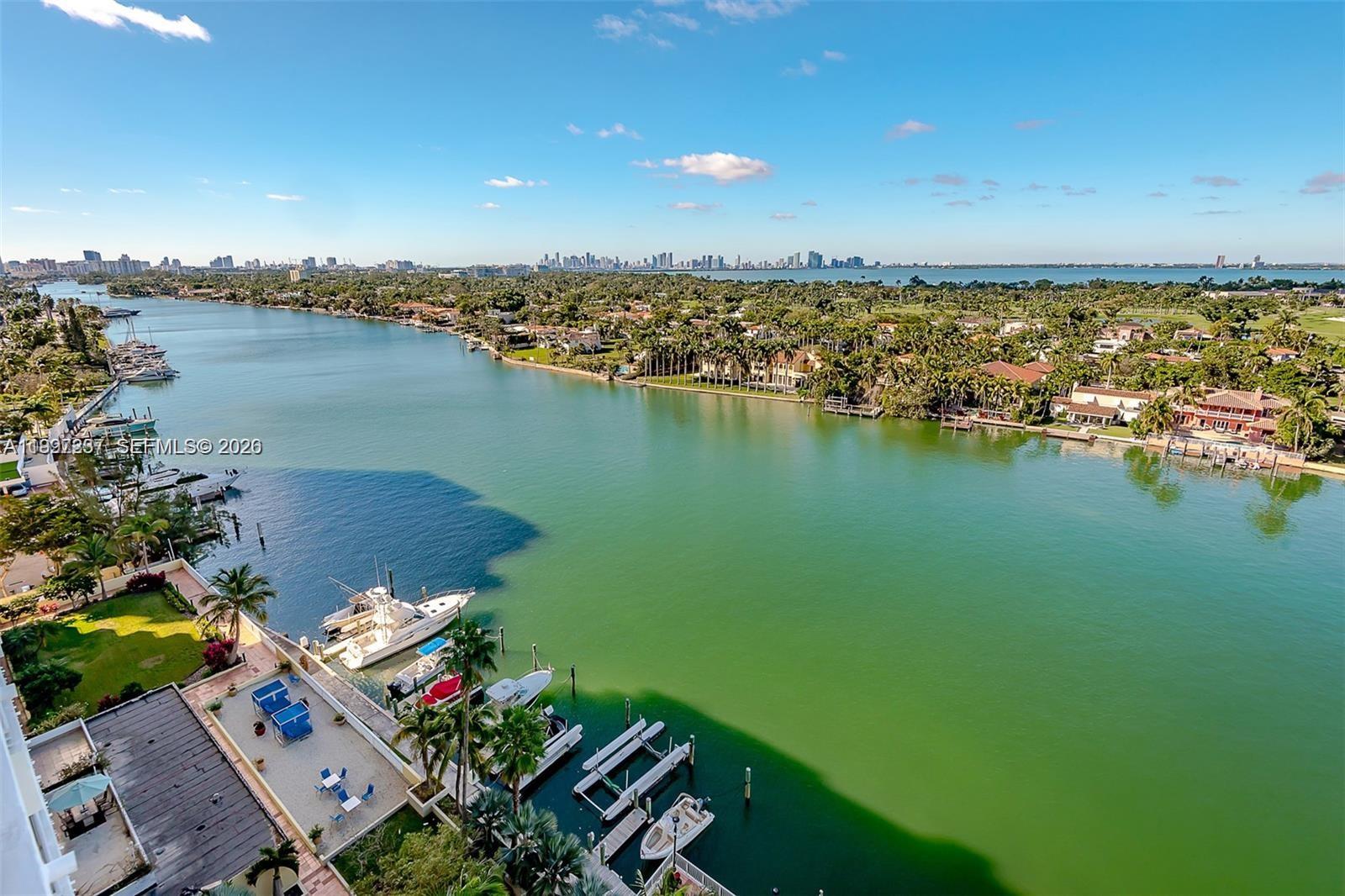 An aerial view shows a waterway lined with houses, docks, and boats under a blue sky — 5600 Collins Ave # 16N, Miami Beach FL 33140, MIAMI BEACH, FL