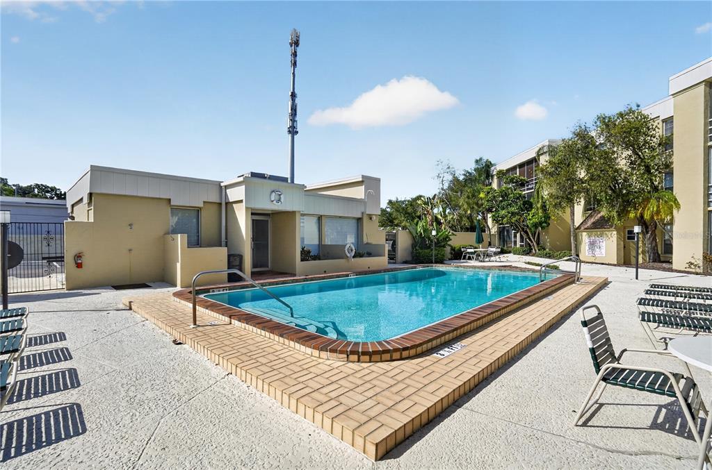 An outdoor swimming pool with a brick border sits in front of a multi-story apartment building — 2302 S MANHATTAN AVENUE UNIT 214, TAMPA, FL