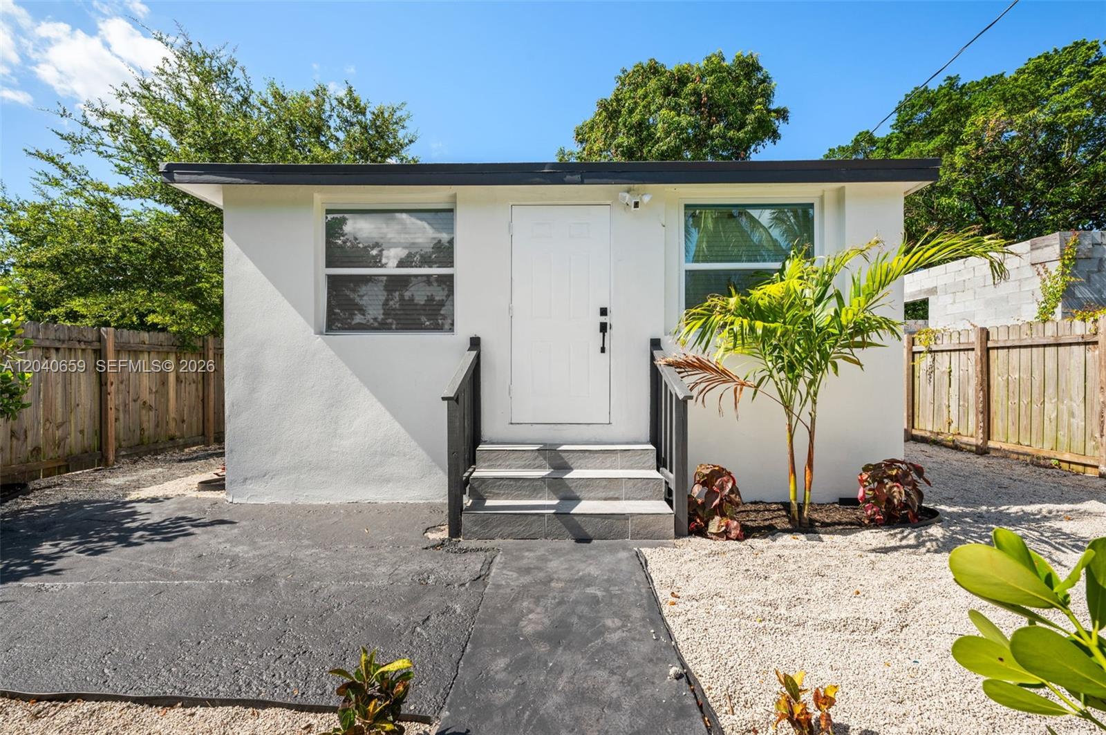 A small, white, single-story house with a flat roof, front steps, and a gravel yard — 1820 NW 63rd St, Miami FL 33147, MIAMI, FL