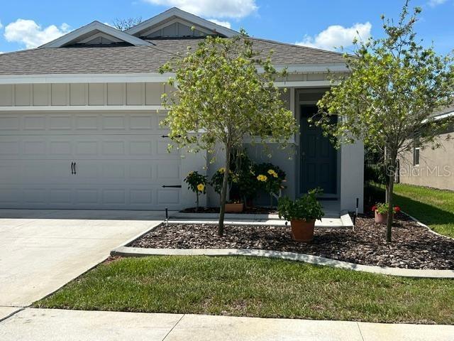 A side view of a single-story house with a garage, gray siding, and landscaping — 5089 STOKES WAY, WILDWOOD, FL