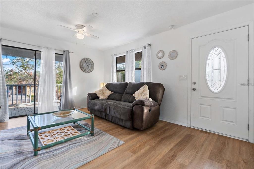 A living room features a dark sofa, a glass coffee table, wood-look flooring, and a door — 1244 31ST AVENUE E, BRADENTON, FL