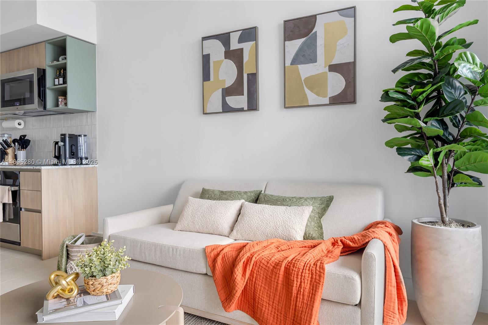 A living area features a light-colored sofa, abstract wall art, and a large potted plant — 159 NE 6TH ST # 2704, Miami FL 33132, MIAMI, FL