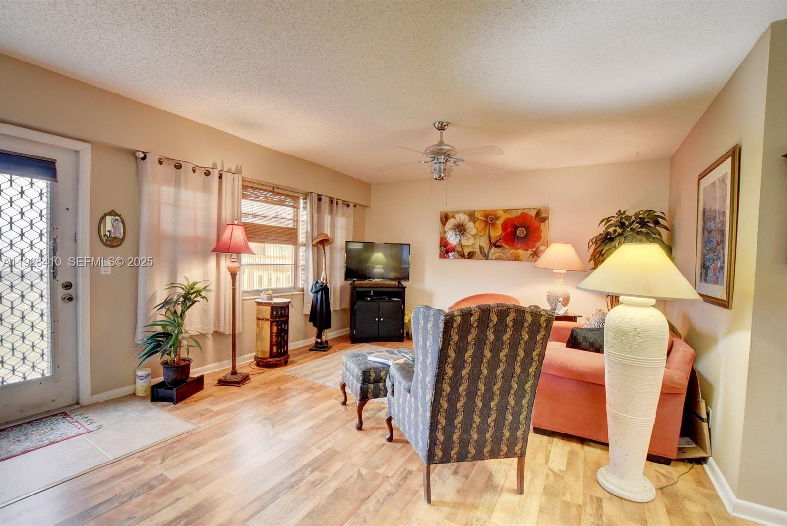 A living room features wood-look flooring, a patterned armchair, a sofa, and a ceiling fan — 293 Mansfield G # 293, Boca Raton FL 33434, BOCA RATON, FL