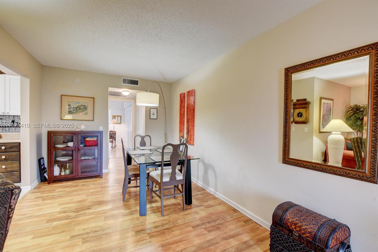 A dining room features a glass-top table, wood flooring, and a large wall mirror — 293 Mansfield G # 293, Boca Raton FL 33434, BOCA RATON, FL