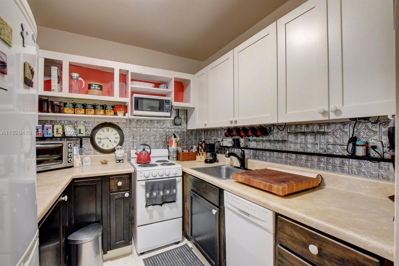 A kitchen features white upper cabinets, dark lower cabinets, a metal backsplash, and a white stove — 293 Mansfield G # 293, Boca Raton FL 33434, BOCA RATON, FL