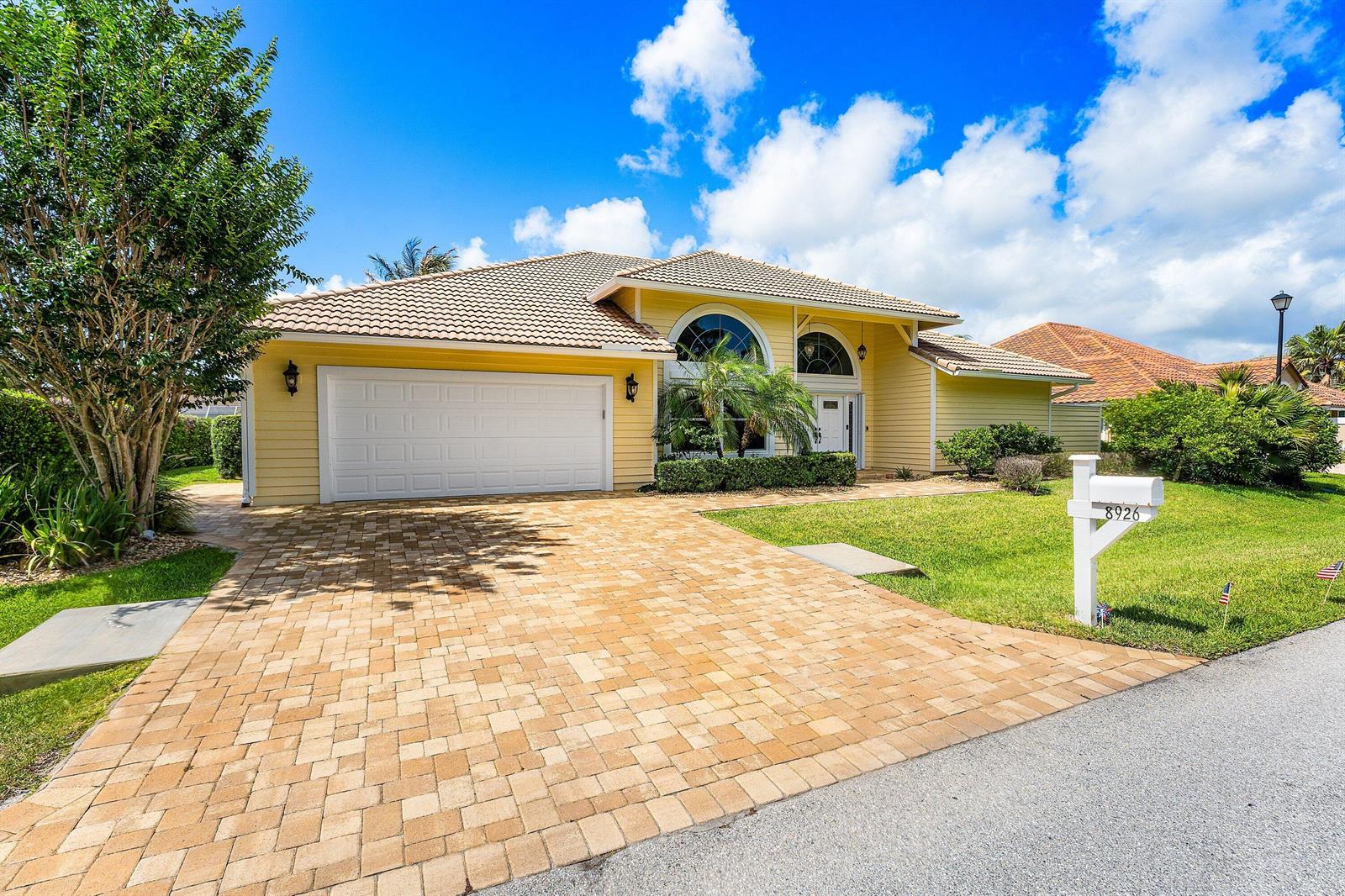 A yellow single-story house with a paved driveway, a two-car garage, and a white mailbox — 8926 SE North Passage Way, Jupiter FL 33469, JUPITER, FL