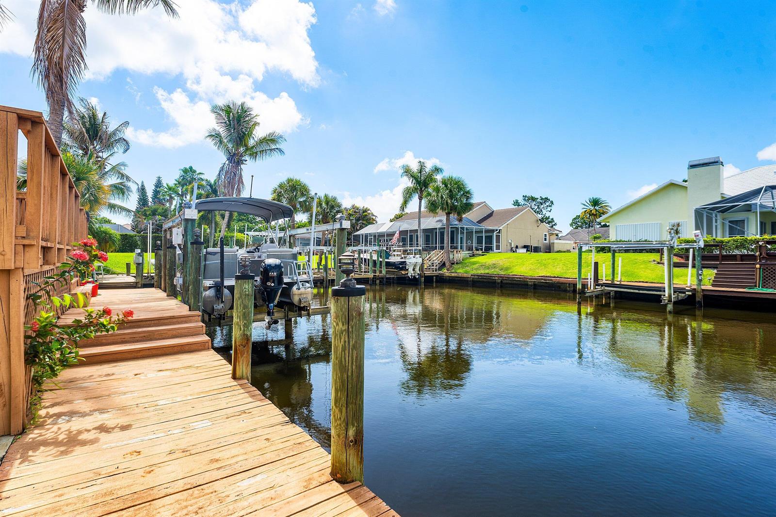 A wooden dock extends along a canal with a boat lift and residential houses nearby — 8926 SE North Passage Way, Jupiter FL 33469, JUPITER, FL