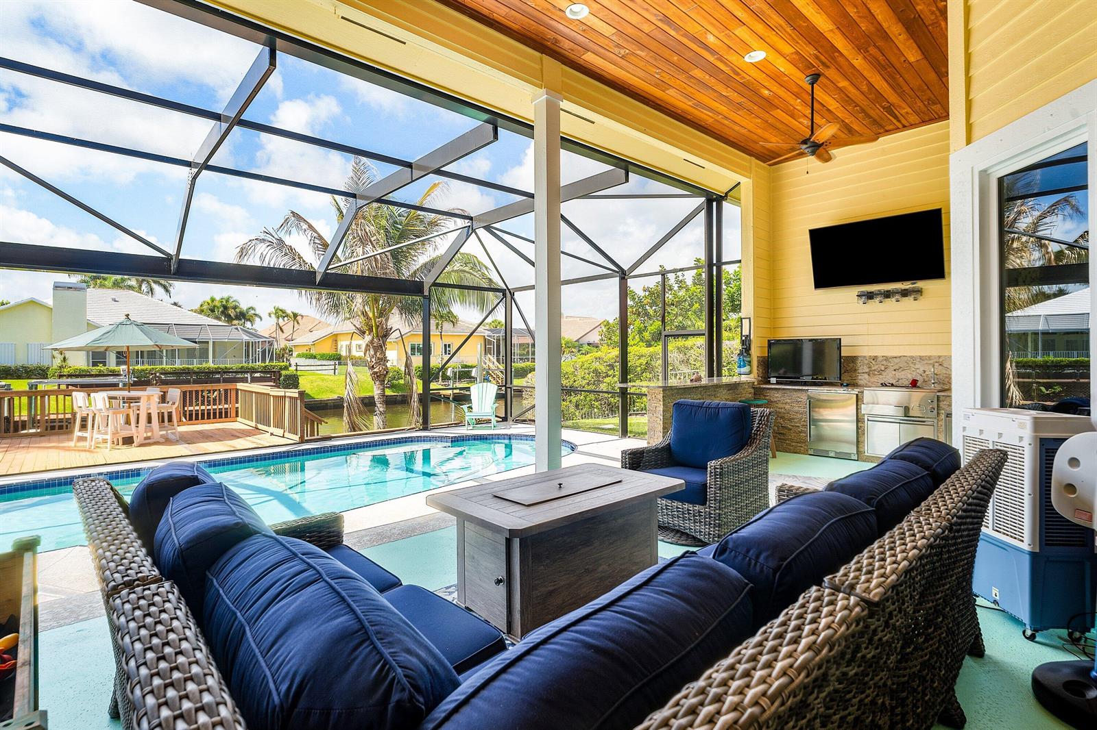 A covered patio features a pool, outdoor kitchen, fire pit, and blue cushioned wicker furniture — 8926 SE North Passage Way, Jupiter FL 33469, JUPITER, FL
