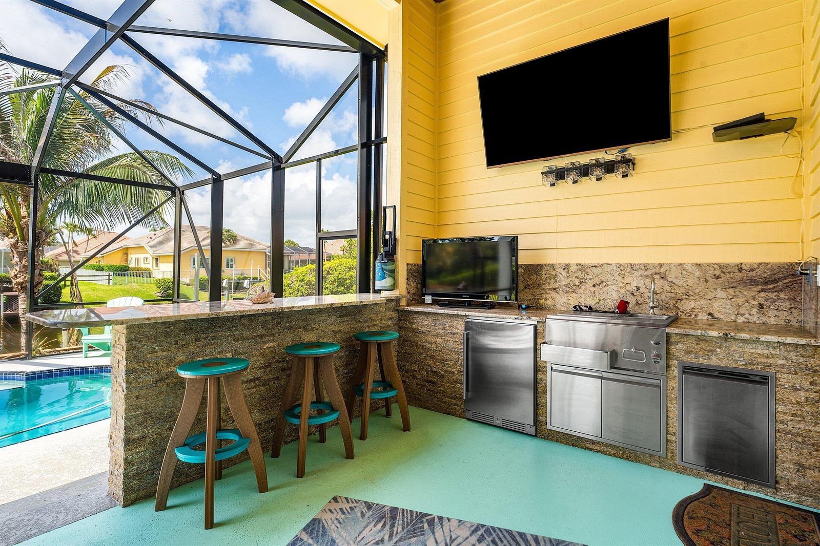 An outdoor kitchen with a bar, stools, stainless steel appliances, and a pool view — 8926 SE North Passage Way, Jupiter FL 33469, JUPITER, FL