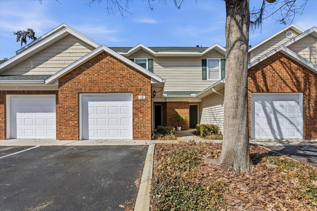 A multi-unit residential building with brick and siding facades, three garage doors, and a tree — 13200 W NEWBERRY ROAD UNIT 86, NEWBERRY, FL