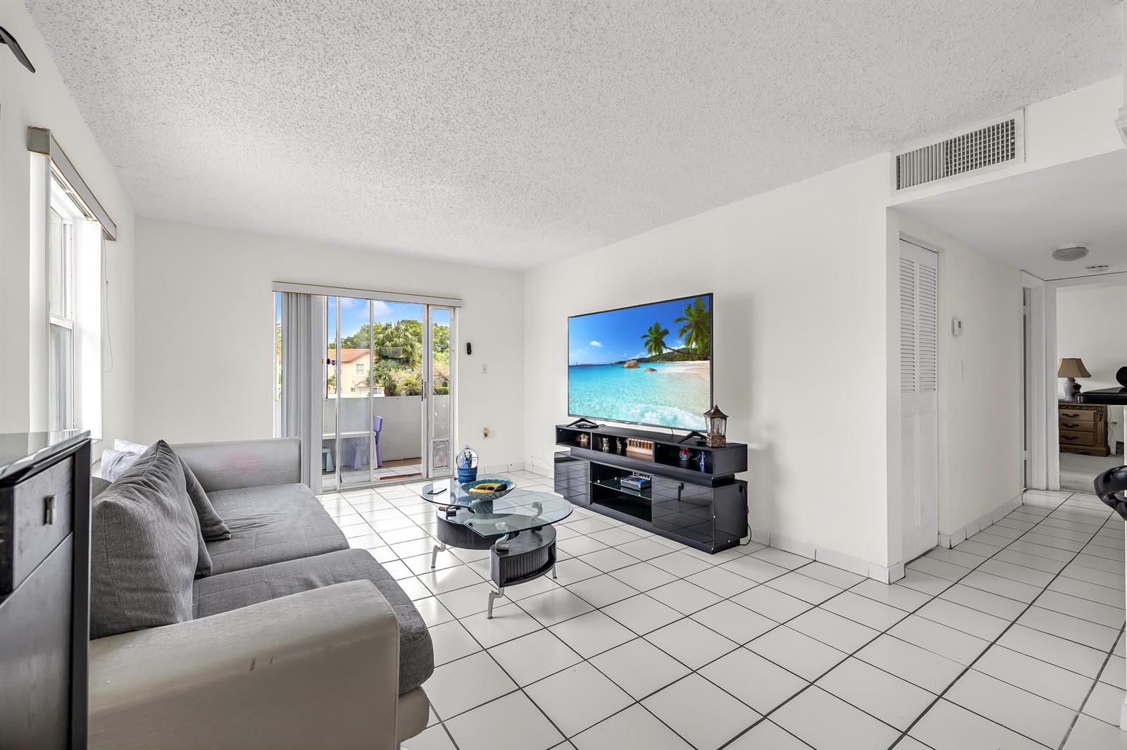 A living room with white tile floors, a grey sofa, a glass coffee table, and a television — 6507 Winfield Boulevard, Margate FL 33063, MARGATE, FL