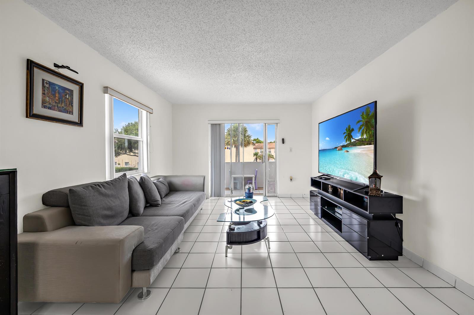 A living room features a grey sofa, glass coffee table, media console, and white tile flooring — 6507 Winfield Boulevard, Margate FL 33063, MARGATE, FL