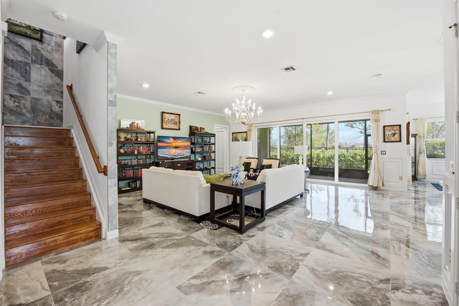 A living room features marble flooring, a wooden staircase, a chandelier, and large sliding glass doors — 984 Sterling Pine Place, Loxahatchee FL 33470, LOXAHATCHEE, FL
