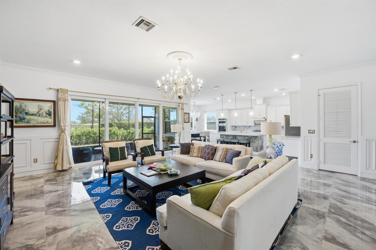 A bright, open-concept living room features marble floors, a large blue area rug, and a chandelier — 984 Sterling Pine Place, Loxahatchee FL 33470, LOXAHATCHEE, FL