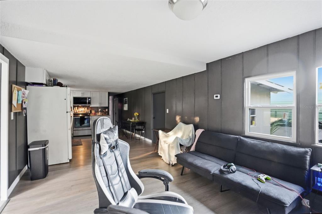 A living room with dark paneled walls, wood-look flooring, a gaming chair, and a sofa — 2085 S STONEBROOK DRIVE, HOMOSASSA, FL