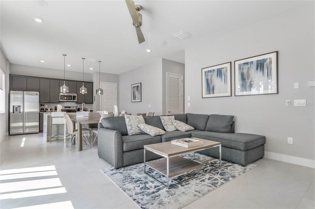 A modern open-concept living room and kitchen featuring a gray sectional sofa and stainless appliances — 7770 SANDY RIDGE DRIVE UNIT 112, REUNION, FL