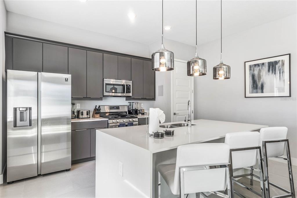 A modern kitchen features dark gray cabinetry, stainless steel appliances, and a white quartz island — 7770 SANDY RIDGE DRIVE UNIT 112, REUNION, FL