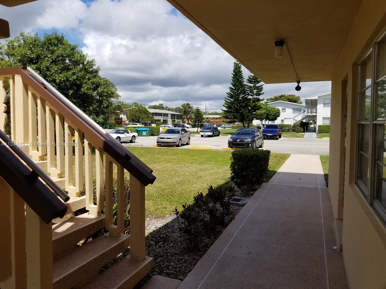 A view from a covered walkway looking out toward a parking lot and apartment buildings — 206 Sheffield I # 206, West Palm Beach FL 33417, WEST PALM BEACH, FL