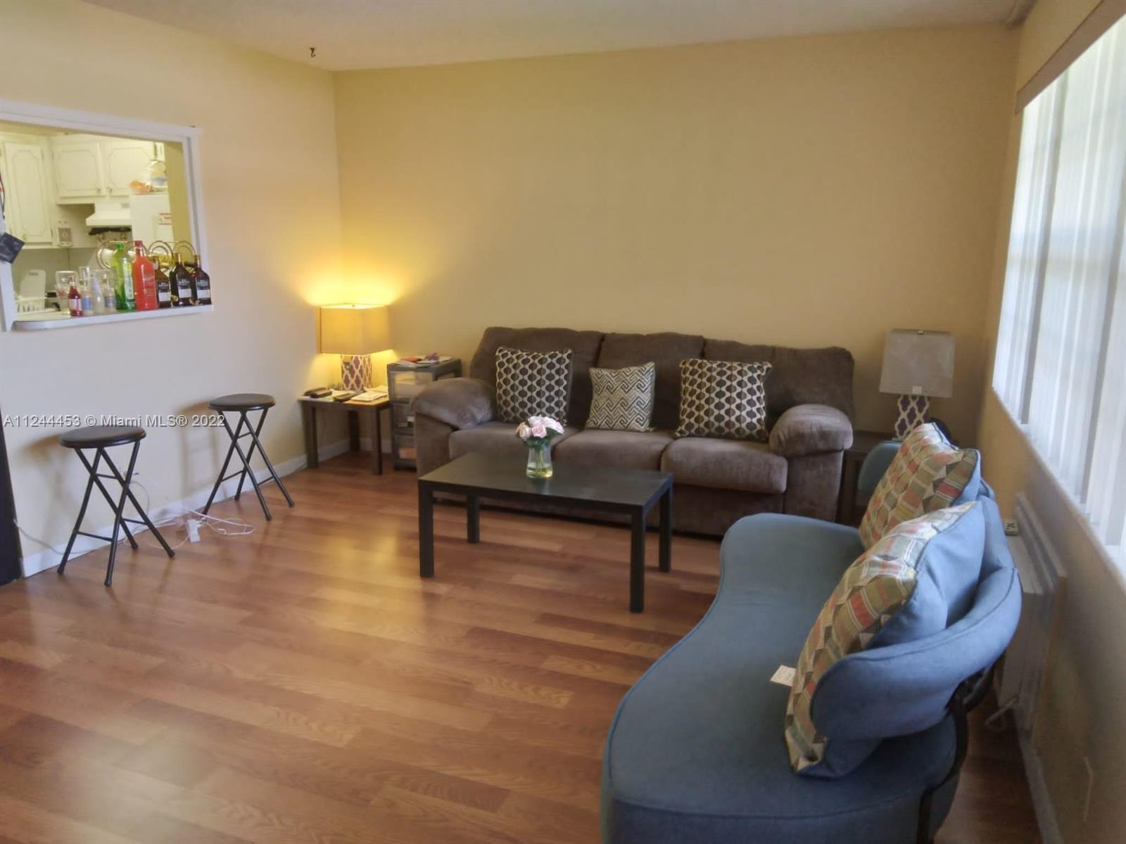 A living room features wood-look flooring, a brown sofa, a blue curved loveseat, and stools — 206 Sheffield I # 206, West Palm Beach FL 33417, WEST PALM BEACH, FL