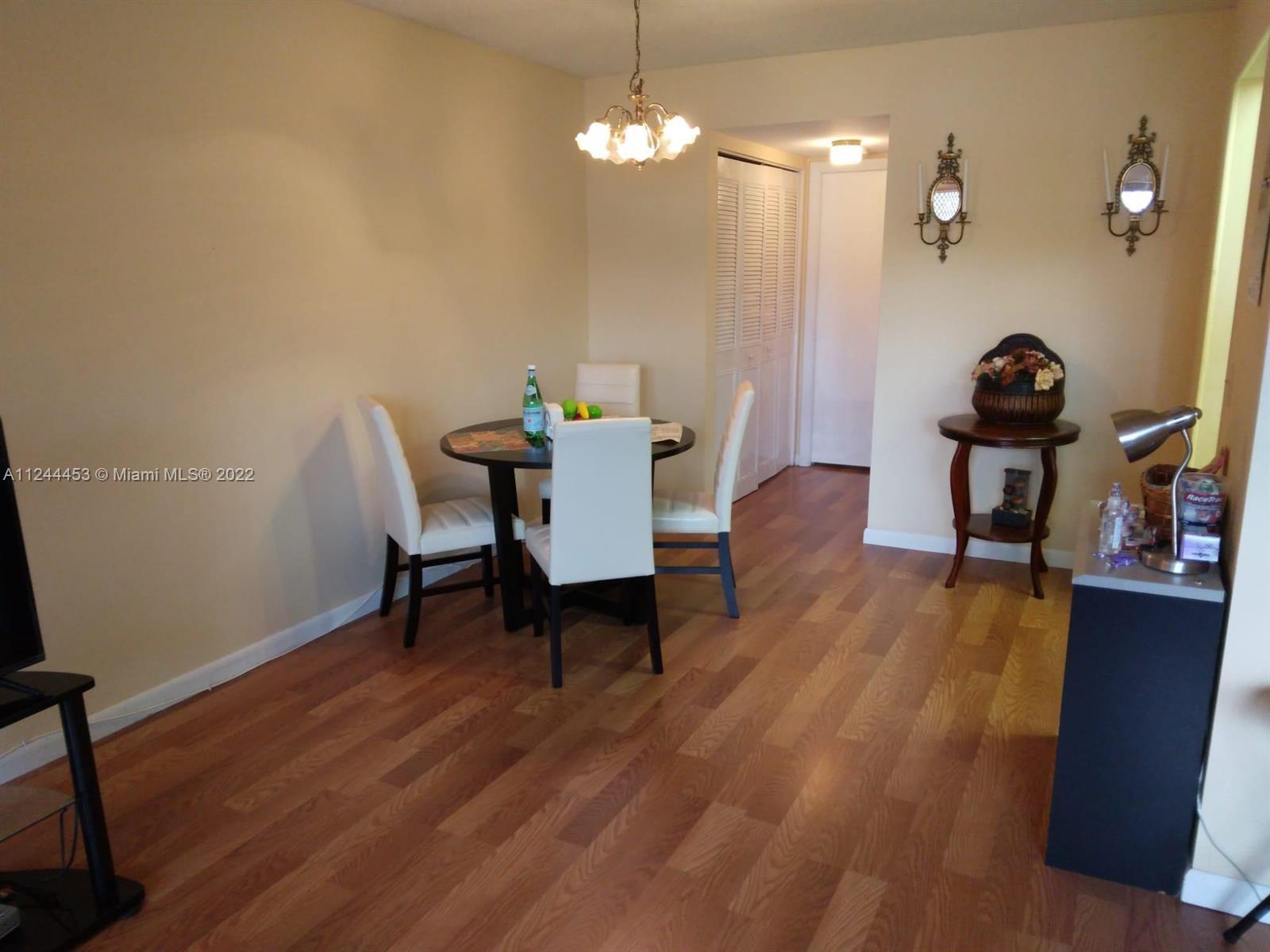 A dining area features a round table with three white chairs and wood-look flooring — 206 Sheffield I # 206, West Palm Beach FL 33417, WEST PALM BEACH, FL