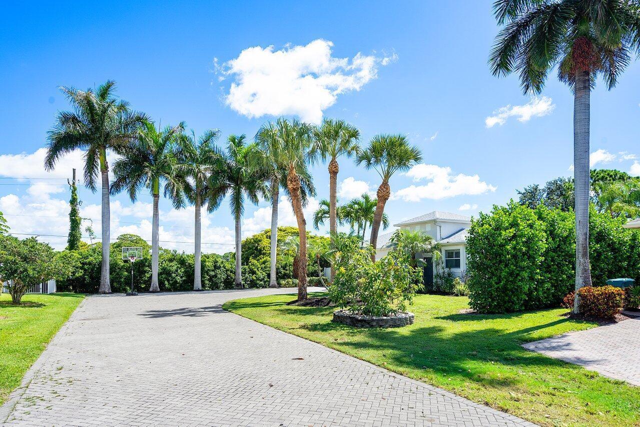 A paved driveway leads to a house surrounded by palm trees under a blue sky — 50 Lake Eden Drive, Boynton Beach FL 33435, BOYNTON BEACH, FL