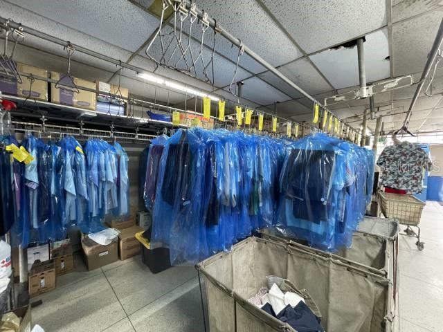 Rows of dry-cleaned garments in blue plastic bags hang above large laundry carts — 400 AV. ING. MANUEL DOMENECH, SAN JUAN, PR