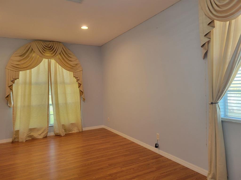 An empty room with light blue walls, wood-look flooring, and two windows with draped curtains — 30541 NORSEMAN PLACE, WESLEY CHAPEL, FL