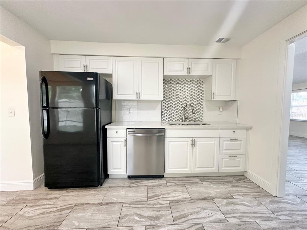 A kitchen features white cabinets, a black refrigerator, stainless steel dishwasher, and patterned tile backsplash — 122 S BULOVA DRIVE, APOPKA, FL