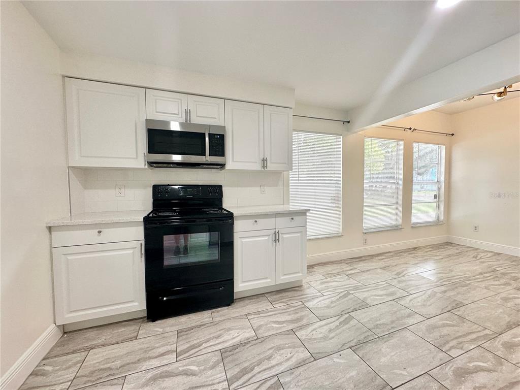 A kitchen with white cabinets, stainless steel microwave, black stove, and light-colored tile flooring — 122 S BULOVA DRIVE, APOPKA, FL