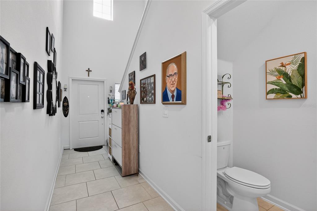 A tiled entryway features a front door, a shoe cabinet, wall art, and a half bathroom — 545 BELL PRAIRIE CIRCLE, LAKE WALES, FL