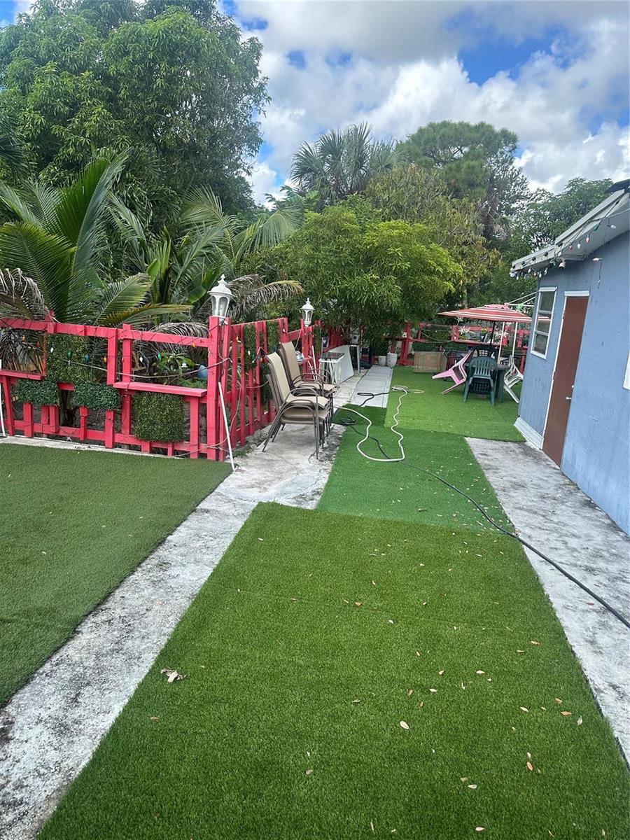 A backyard features artificial turf sections, a red wooden fence, and a blue exterior wall — 541 NW 33rd Avenue, Lauderhill FL 33311, LAUDERHILL, FL