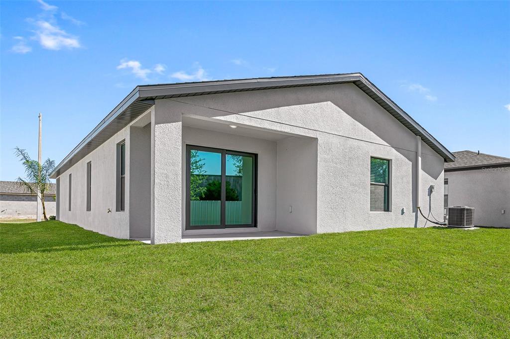 The exterior rear view of a single-story house features a covered patio and lawn — 525 BLACKTHORN DRIVE, LAKELAND, FL