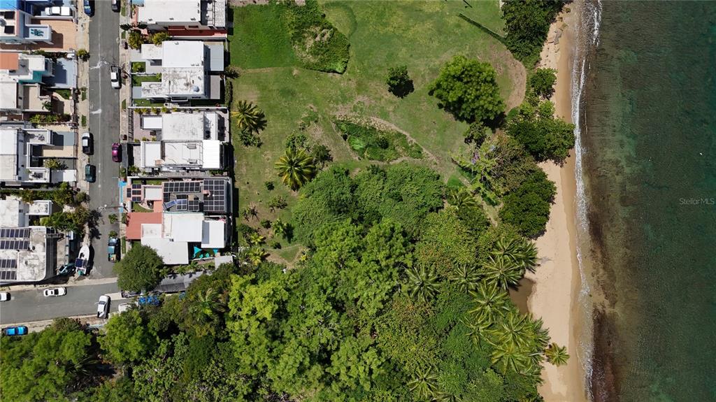 An aerial view shows a coastal property with a grassy lot, trees, and adjacent houses — Calle #2 URB VISTA AZUL UNIT C-22, RINCON, PR