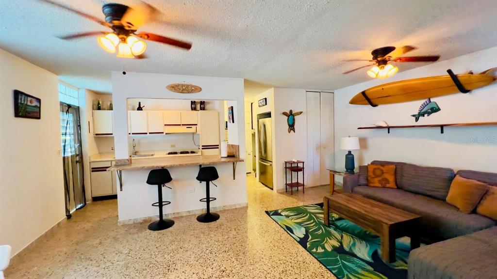 An open-concept living room and kitchen featuring a surfboard wall decoration and terrazzo flooring — Calle #2 URB VISTA AZUL UNIT C-22, RINCON, PR