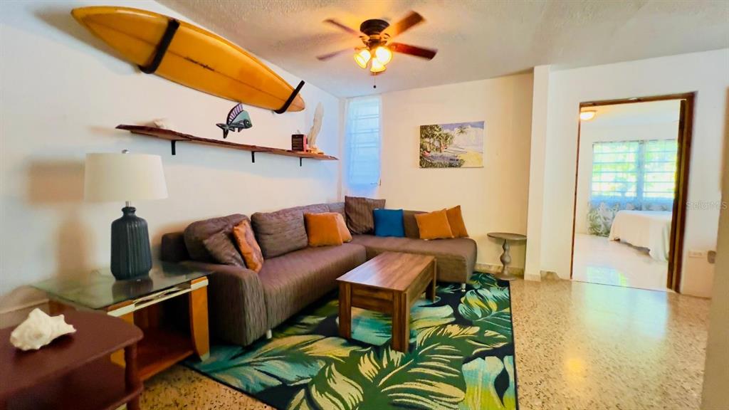 A living room features a sectional sofa, a surfboard wall decoration, and a tropical rug — Calle #2 URB VISTA AZUL UNIT C-22, RINCON, PR